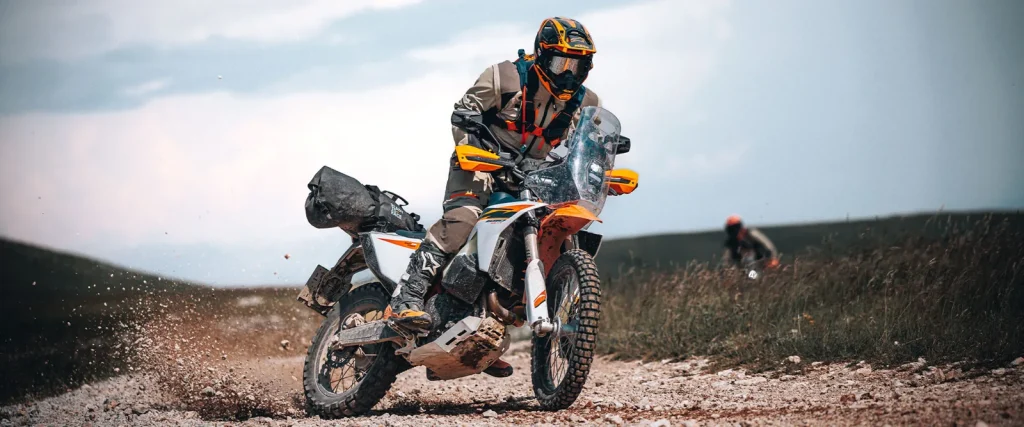 2027 KTM 690 Rally ridden standing on a gravel track, showing the rally tower, windshield, dual front fuel tanks and soft luggage