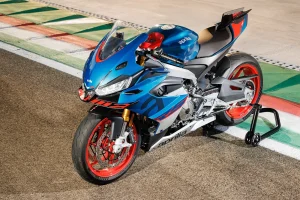High angle view of a blue Aprilia RS 660 Factory with red wheels and gold Ohlins fork parked on a paddock stand beside a painted race-track kerb