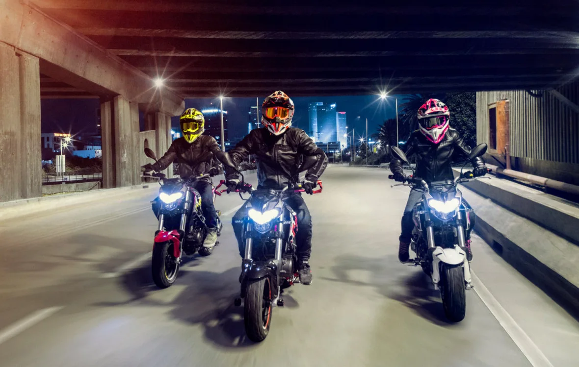 Three riders on Benelli TNT 125s in black, red and white riding side by side under a highway overpass at night
