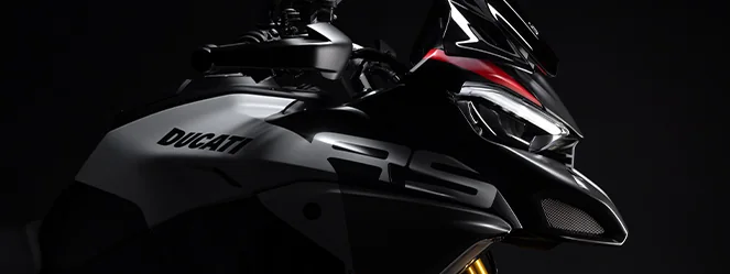 Close-up of the Ducati Diavel V4 RS front end in the dark showing the LED headlight, RS lettering on the tank cover and the Ducati logo