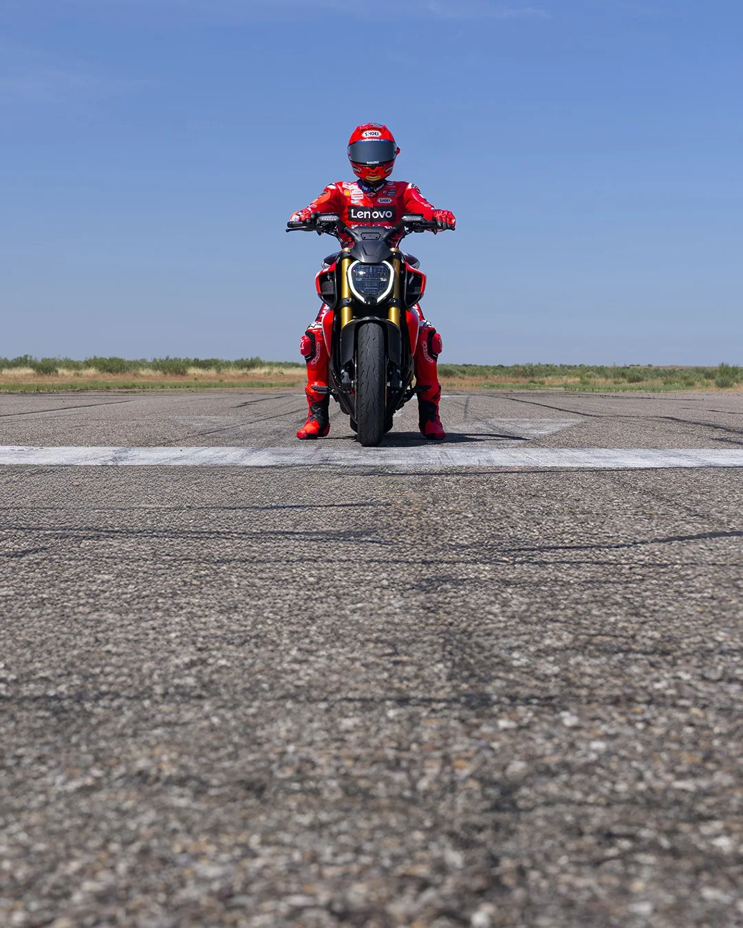 Marc Marquez sitting on a Ducati Diavel V4 RS at a painted line on an airstrip with tyre marks on the tarmac