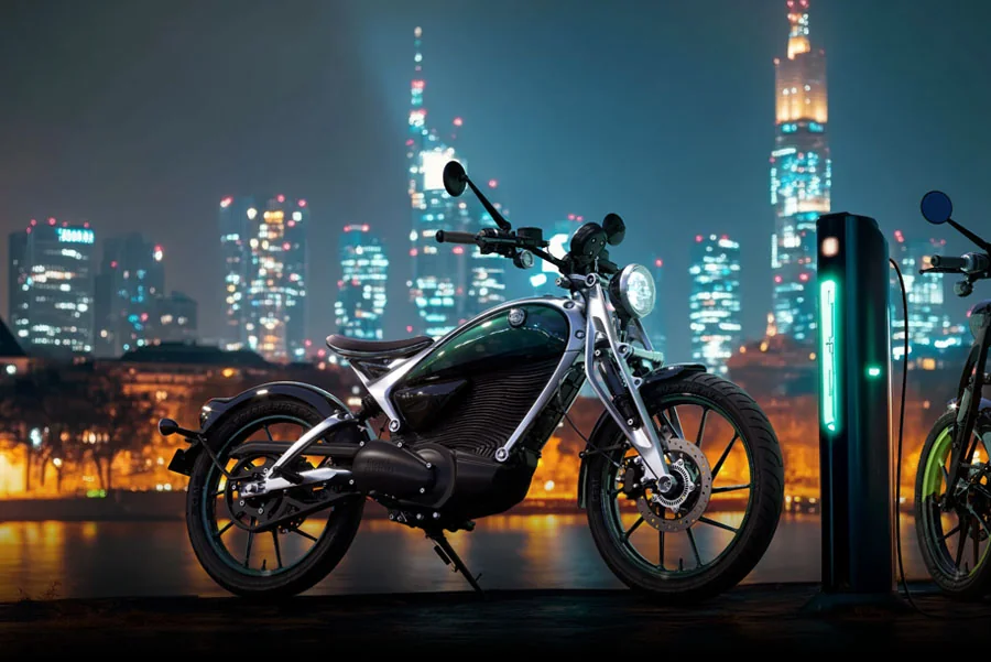 Flying Flea C6 electric motorcycle in Flea Green parked beside a glowing charging post at night with a lit city skyline across the water