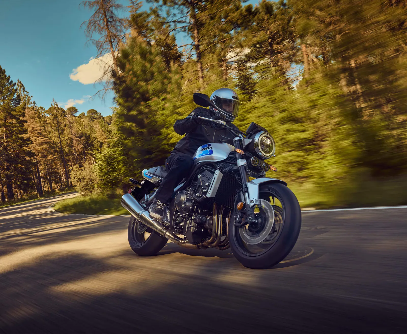 Rider cornering a 2026 Honda CB1000F on a tree-lined road, the bike leaned over with trees blurred behind