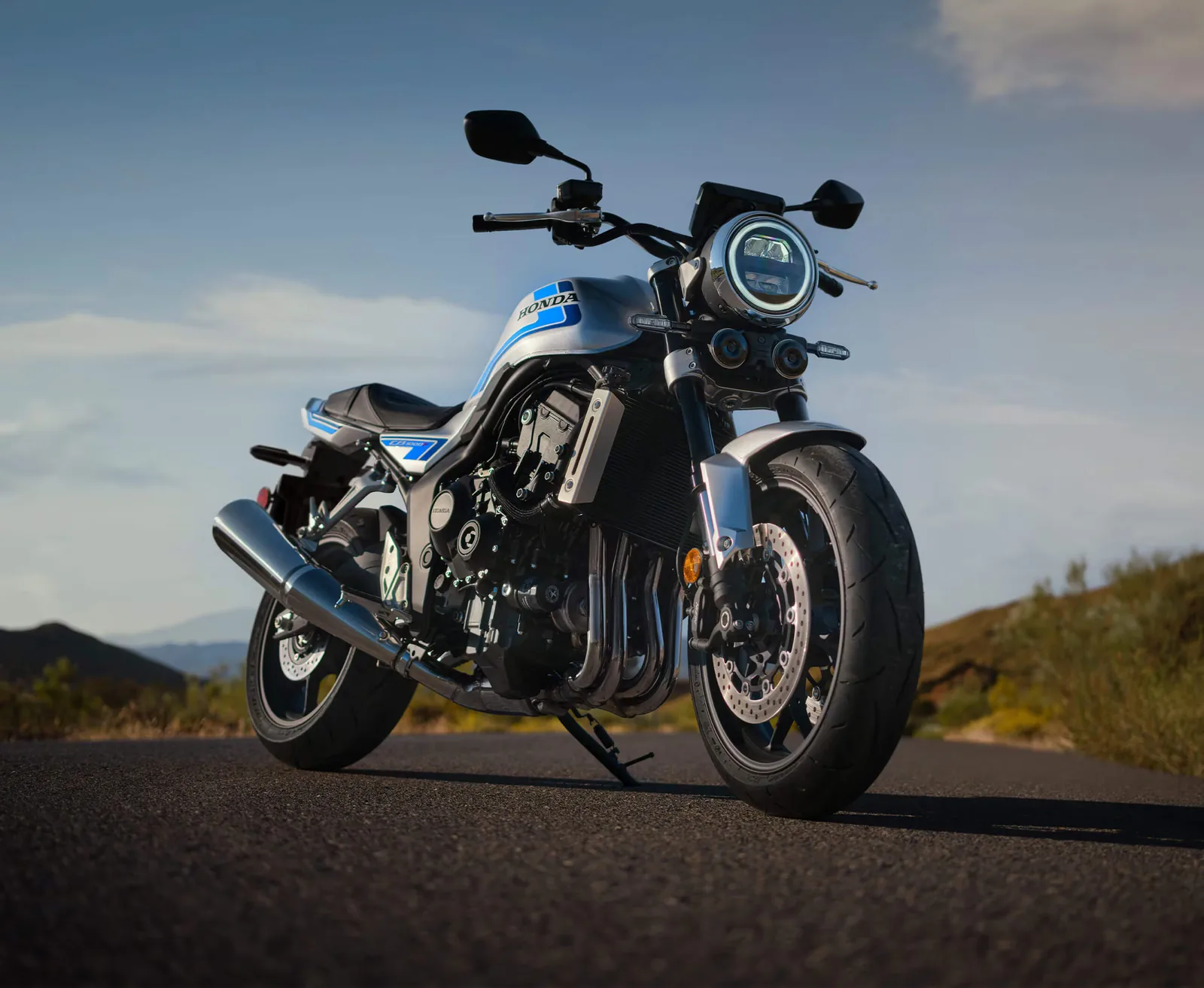 2026 Honda CB1000F in Wolf Silver Metallic with blue stripes, parked on a hill road and seen from the front three-quarter, showing the round LED headlight, upside-down fork and twin front discs