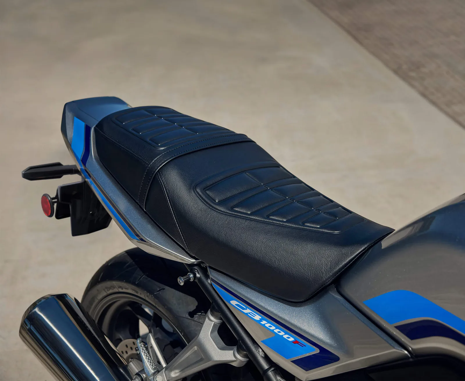Close-up of the stepped, stitched seat and blue-striped tail unit of the 2026 Honda CB1000F with the megaphone silencer below