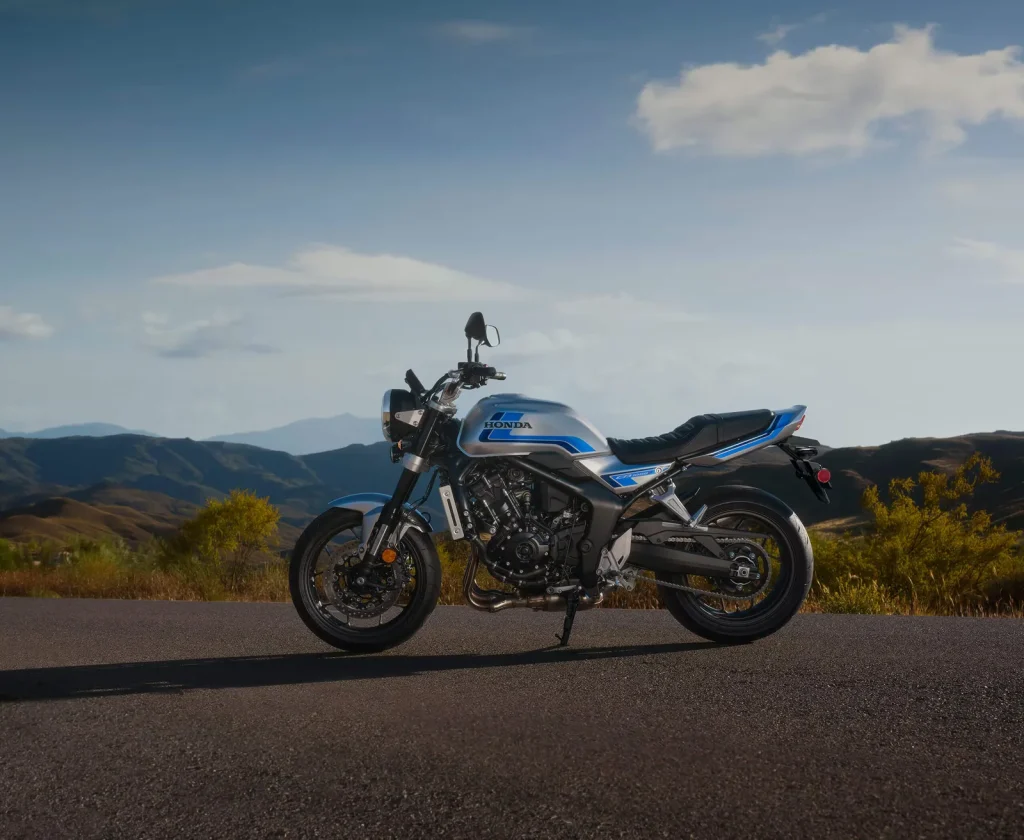 2026 Honda CB1000F parked side-on on a tar road at dusk with hills behind, showing the silver and blue paint, flat seat and 4-into-1 exhaust