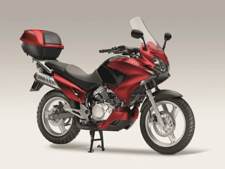 Front three-quarter studio view of the Honda Varadero 125 in Pearl Siena Red with tall screen, half fairing, cast wheels, trail tyres and a Honda top box on the rear rack