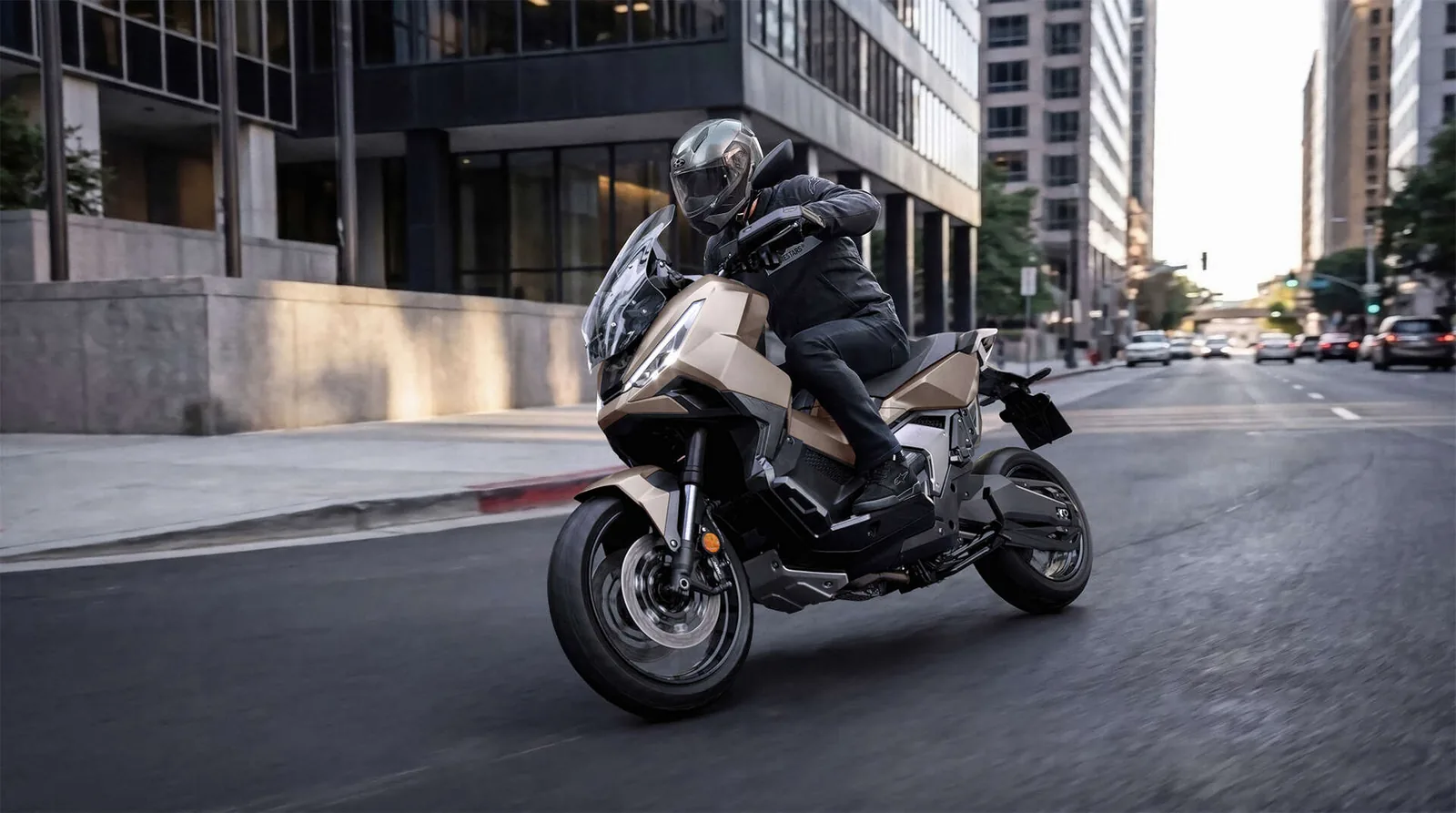 Rider in a modular helmet leaning a gold Honda X-ADV through a city corner with office blocks behind