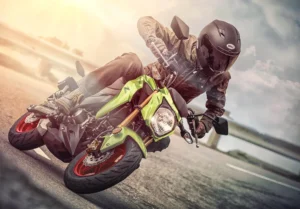 Rider in a black Bell helmet leaning a Metallic Yellowish Green Kawasaki Z125 Pro through a corner on a coastal road, red wheels and gold upside-down fork visible