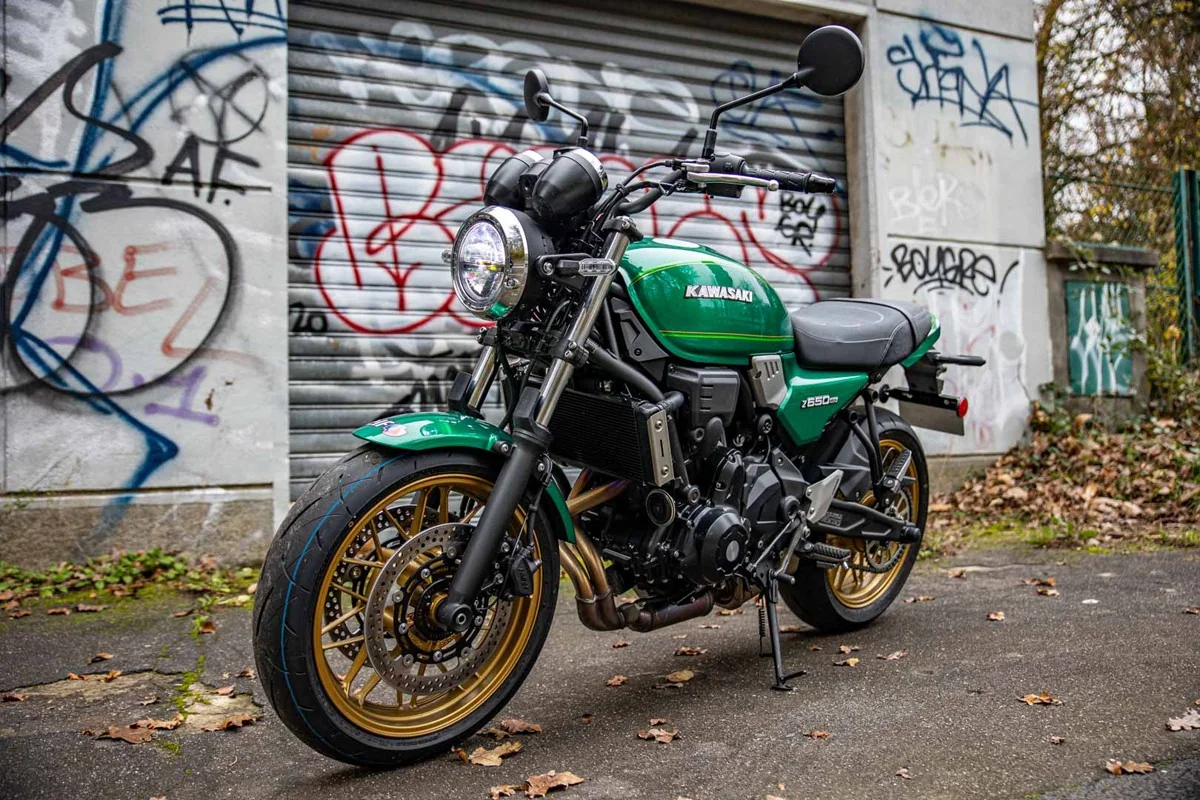 Green Kawasaki Z650RS front three-quarter view with round LED headlight, gold cast wheels and twin front discs, in front of graffiti