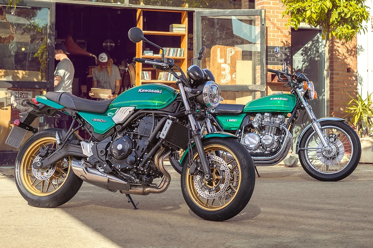 A green Kawasaki Z650RS parked beside an original green Kawasaki Z650 four-cylinder from the 1970s outside a record shop