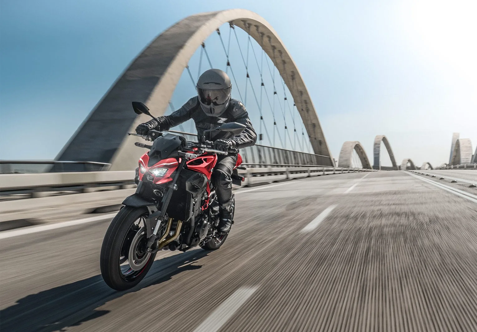 Rider on a red Kawasaki Z900 crossing a bridge with concrete arches at speed