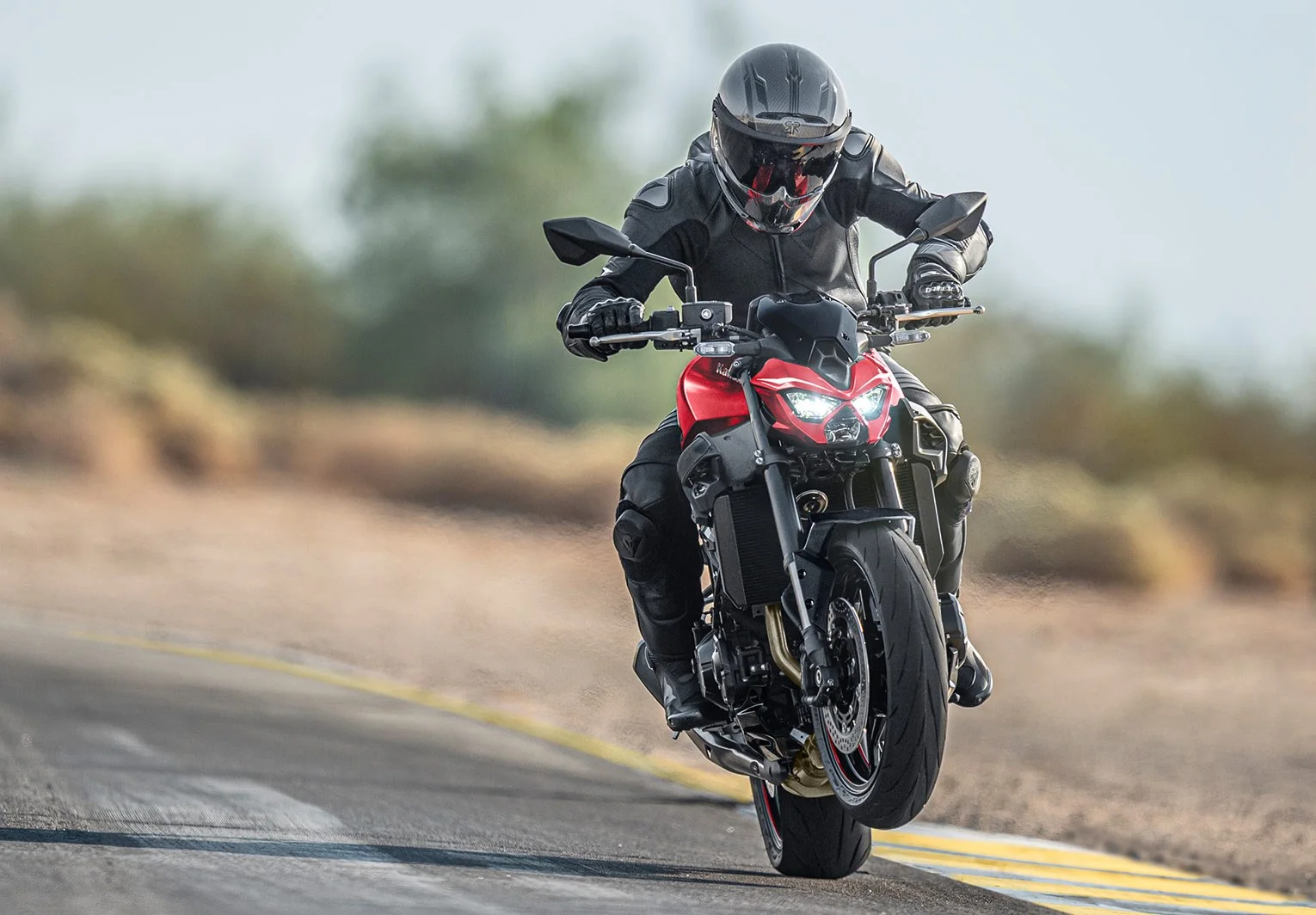 Rider in a carbon helmet wheelying a red Kawasaki Z900 on a race track
