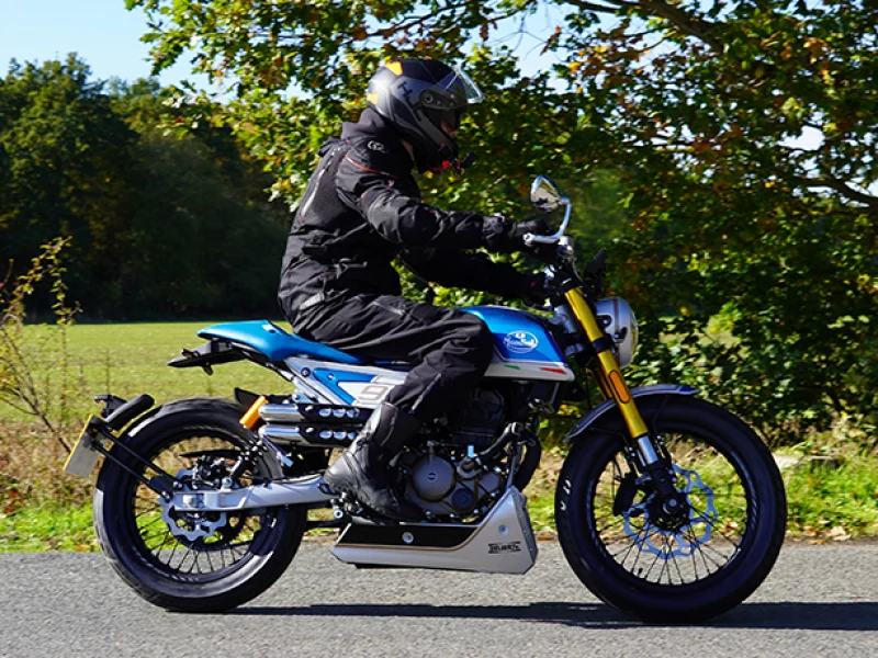 Rider in black textile gear on a silver and light blue Mondial HPS 125 Ubbiali Limited with gold upside-down forks, number 9 side plate and twin shotgun exhausts on a country lane