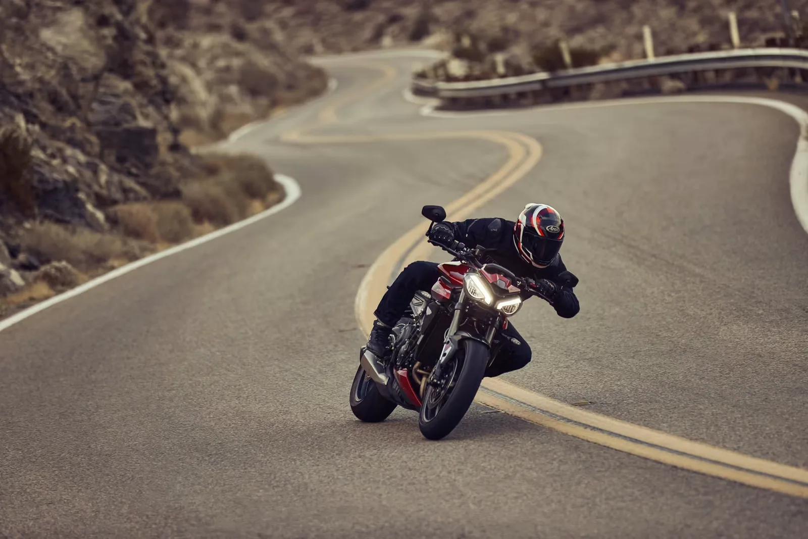 Rider cornering a red and black Triumph Street Triple RS on a winding mountain road