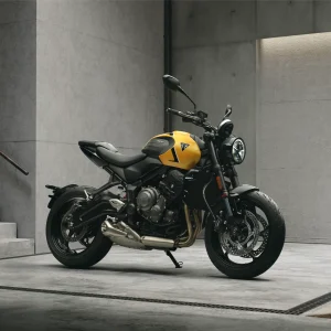 2026 Triumph Trident 660 in Cosmic Yellow parked in a concrete garage, front three-quarter view showing the round headlight, gold fork and three-cylinder engine